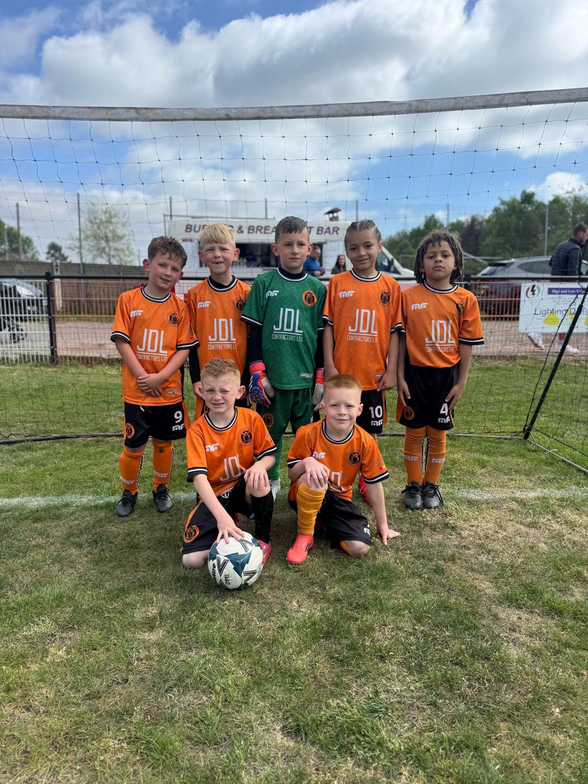 A young team in orange kits lined up in front of a goal with a football