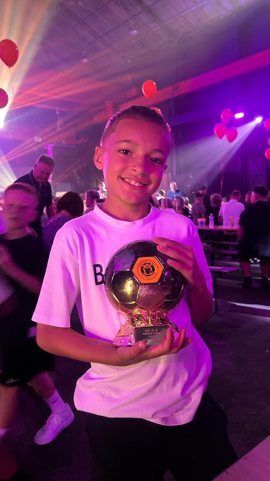 Xander holding a golden ball trophy under stage lights at presentation night