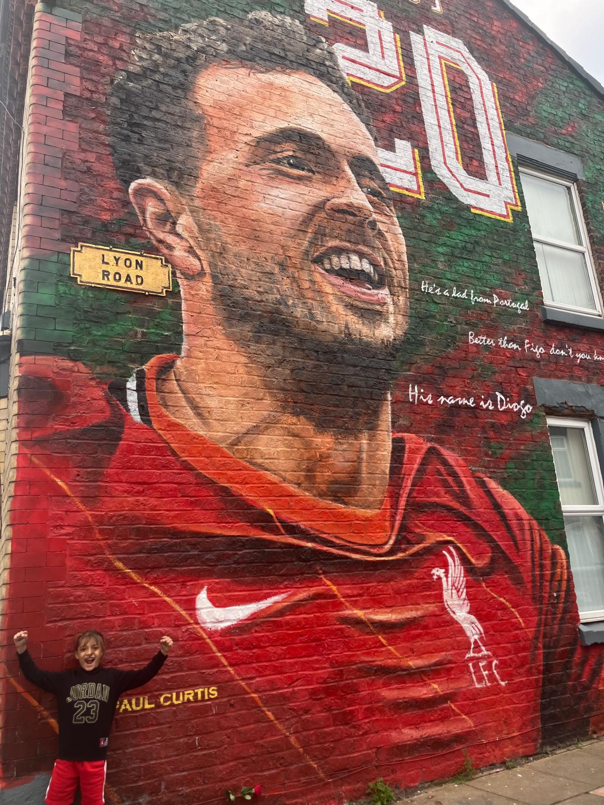 Xander with arms raised in front of a large street mural of a footballer