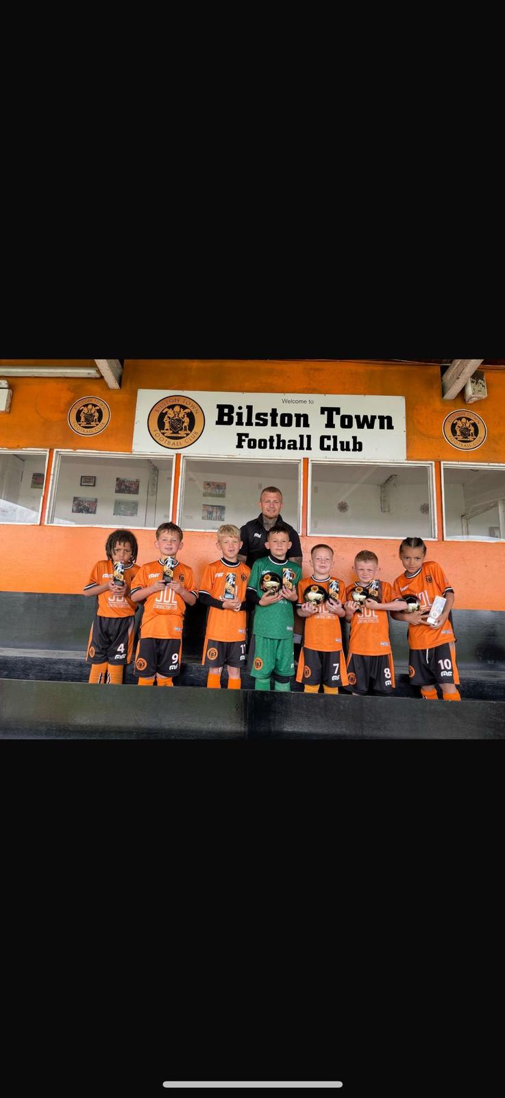 The team holding medals outside the Bilston Town Football Club stand with their coach