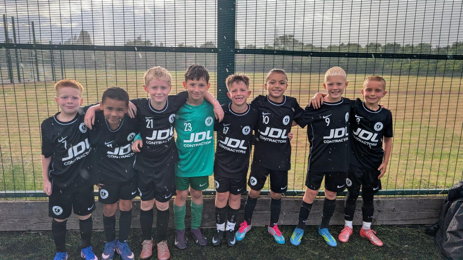 The squad in black kits lined up against a fence in the rain