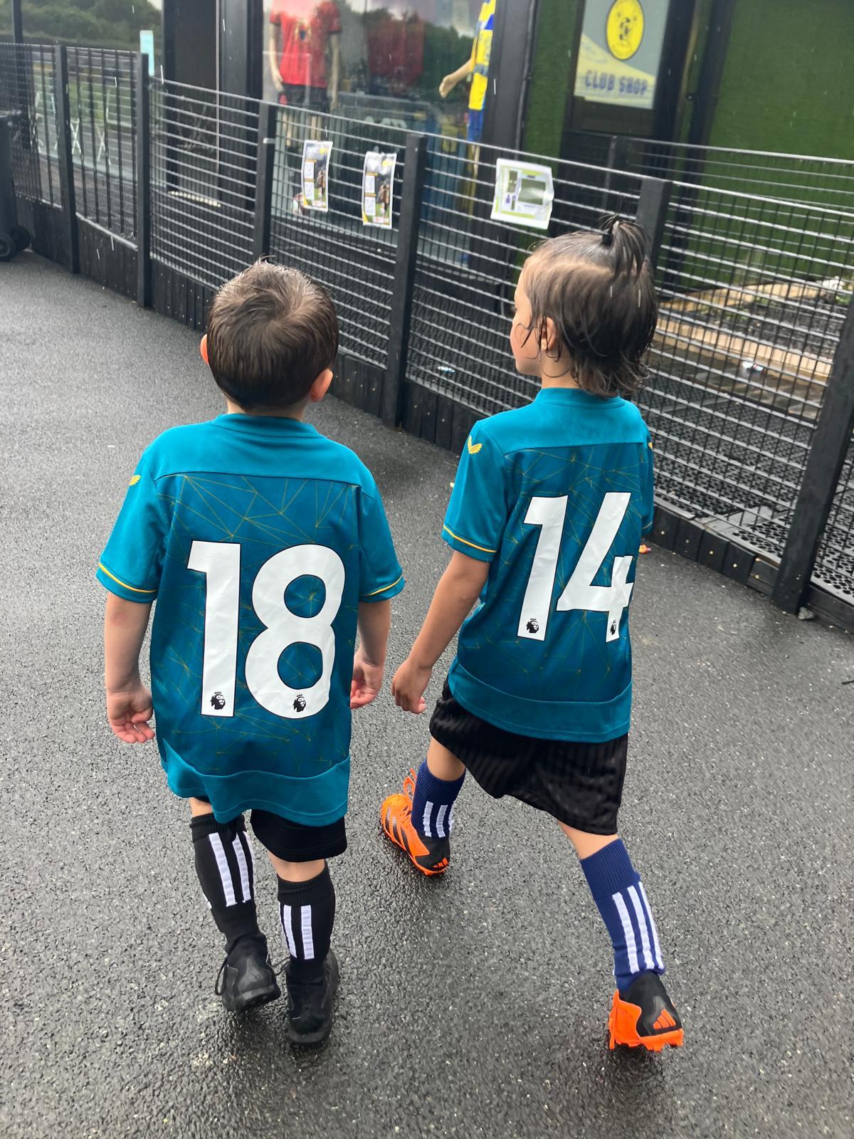 Two young players walking to the pitch in teal shirts, numbers 18 and 14