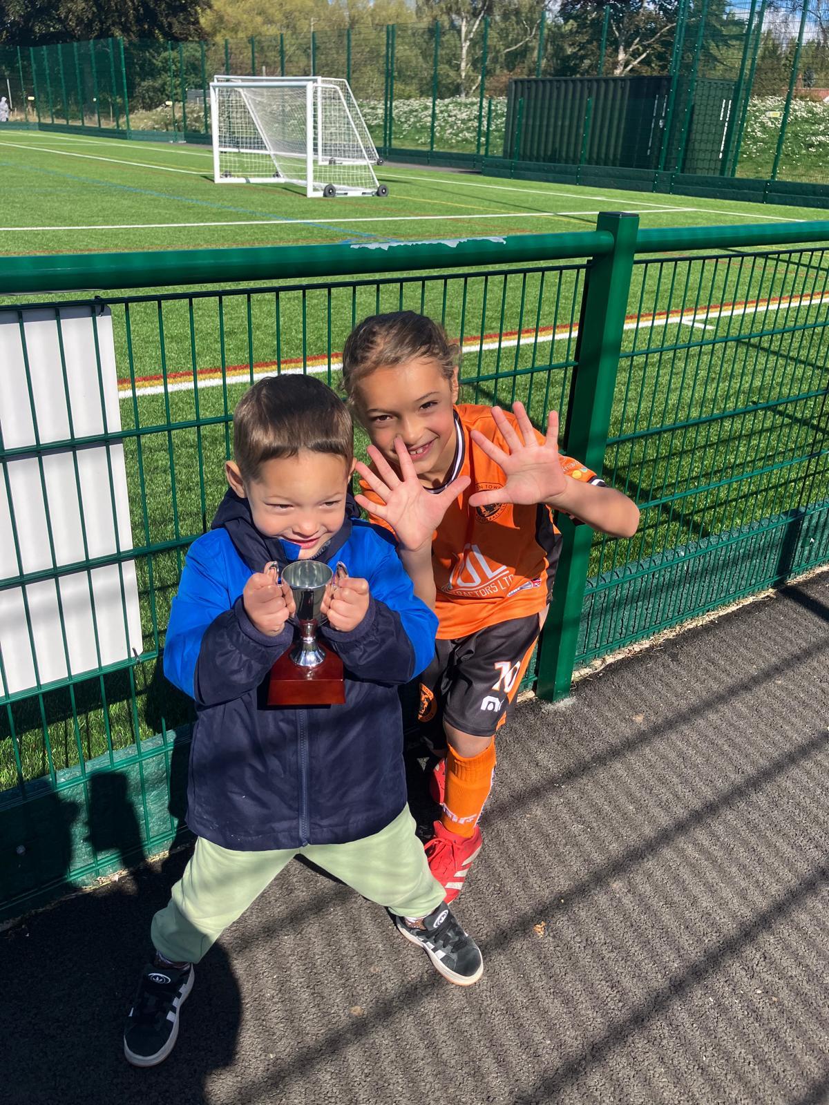 Xander in his orange kit with a younger sibling holding a small silver cup