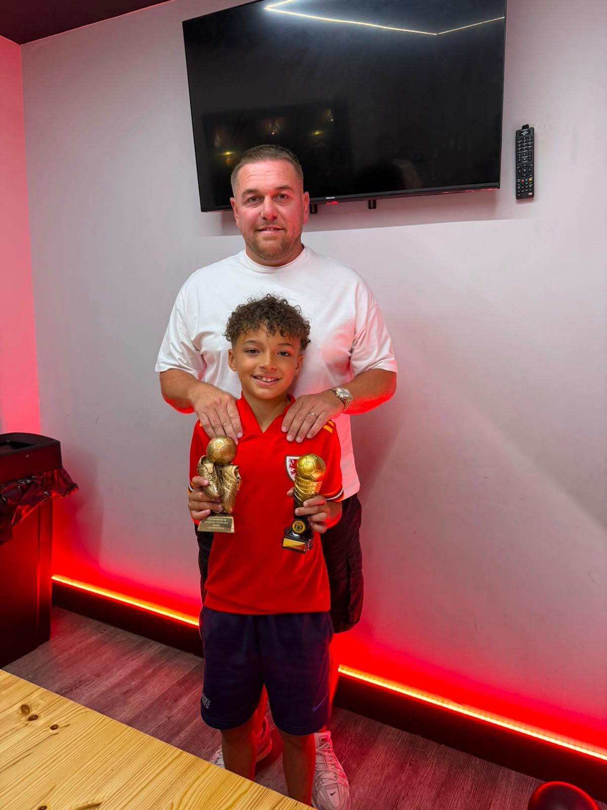 Xander holding his two trophies with a proud family member behind him